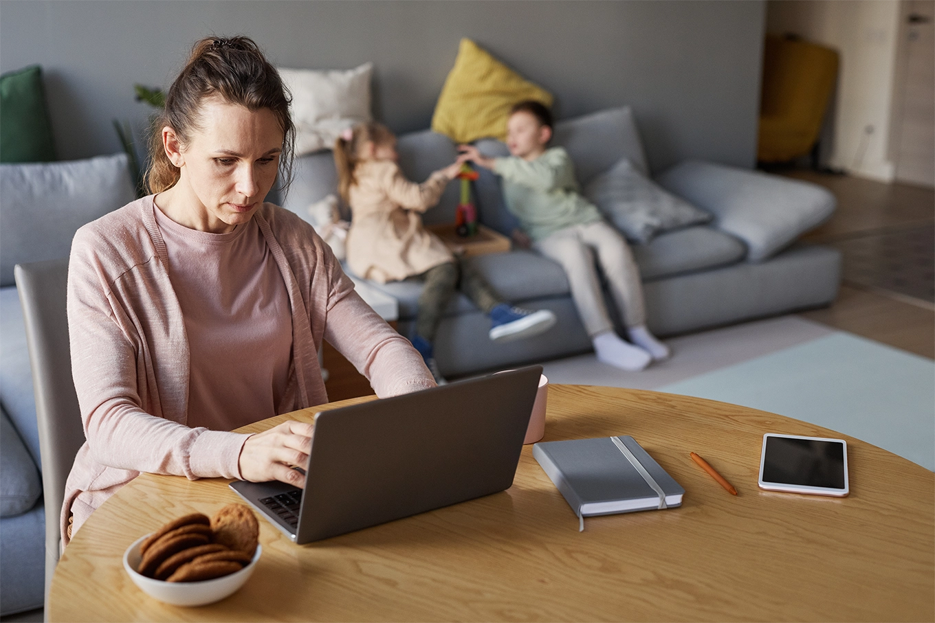 mother working on laptop with children playing on the sofa